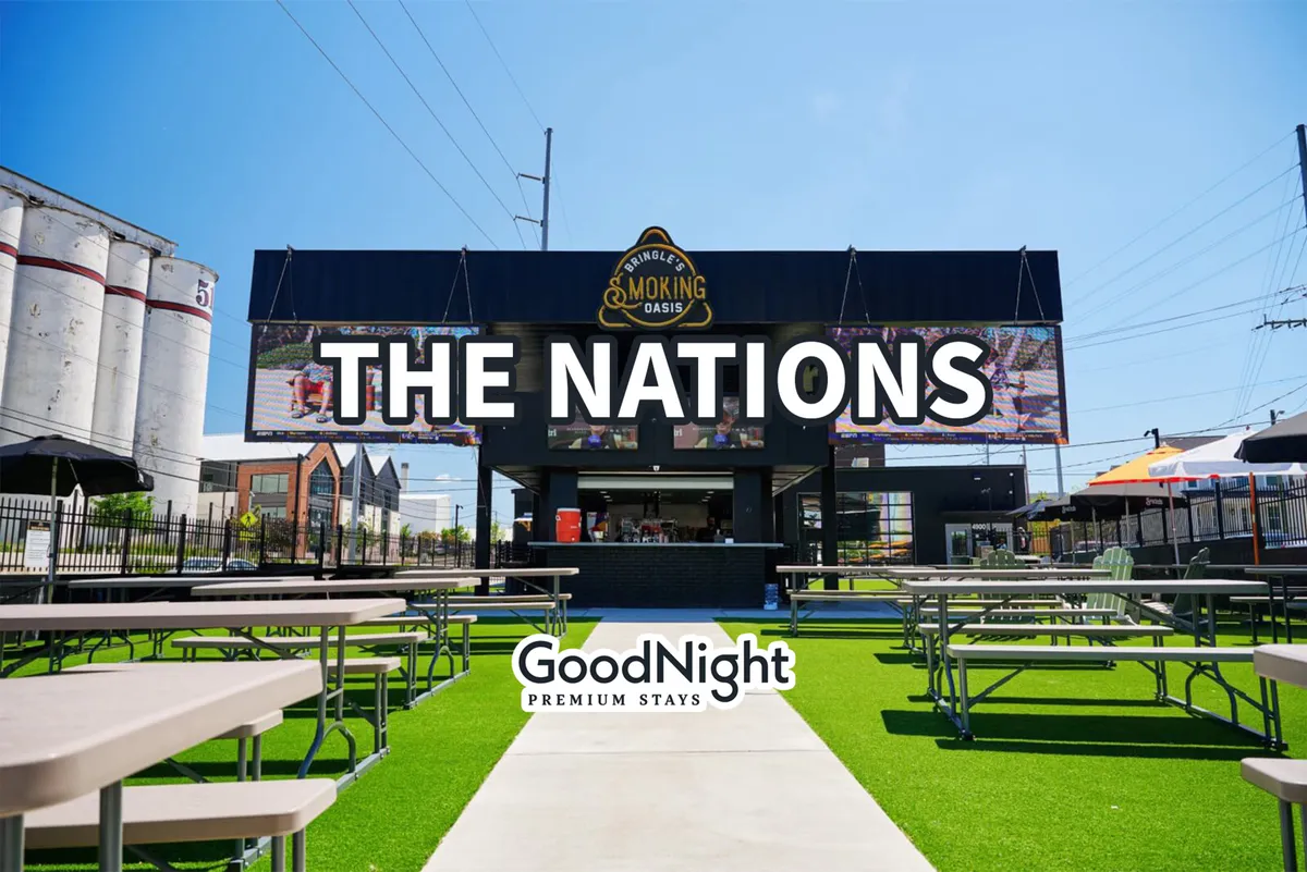 An energetic exterior shot showing 'THE NATIONS' sign, a food service area, outdoor seating with tables, and a grassy area where people can gather. The scene exudes a lively neighborhood vibe with opportunities for dining, socializing, and enjoying themed community events.