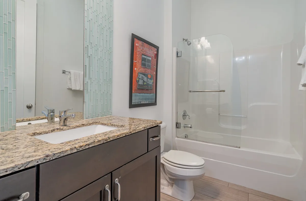 A contemporary bathroom with a granite countertop, colorful wall art, and a clear view of the glass shower enclosure. The scene is stylish yet practical, offering a sense of both relaxation and aesthetic appeal. The inviting atmosphere is enhanced by the thoughtful decor and spotless surfaces.